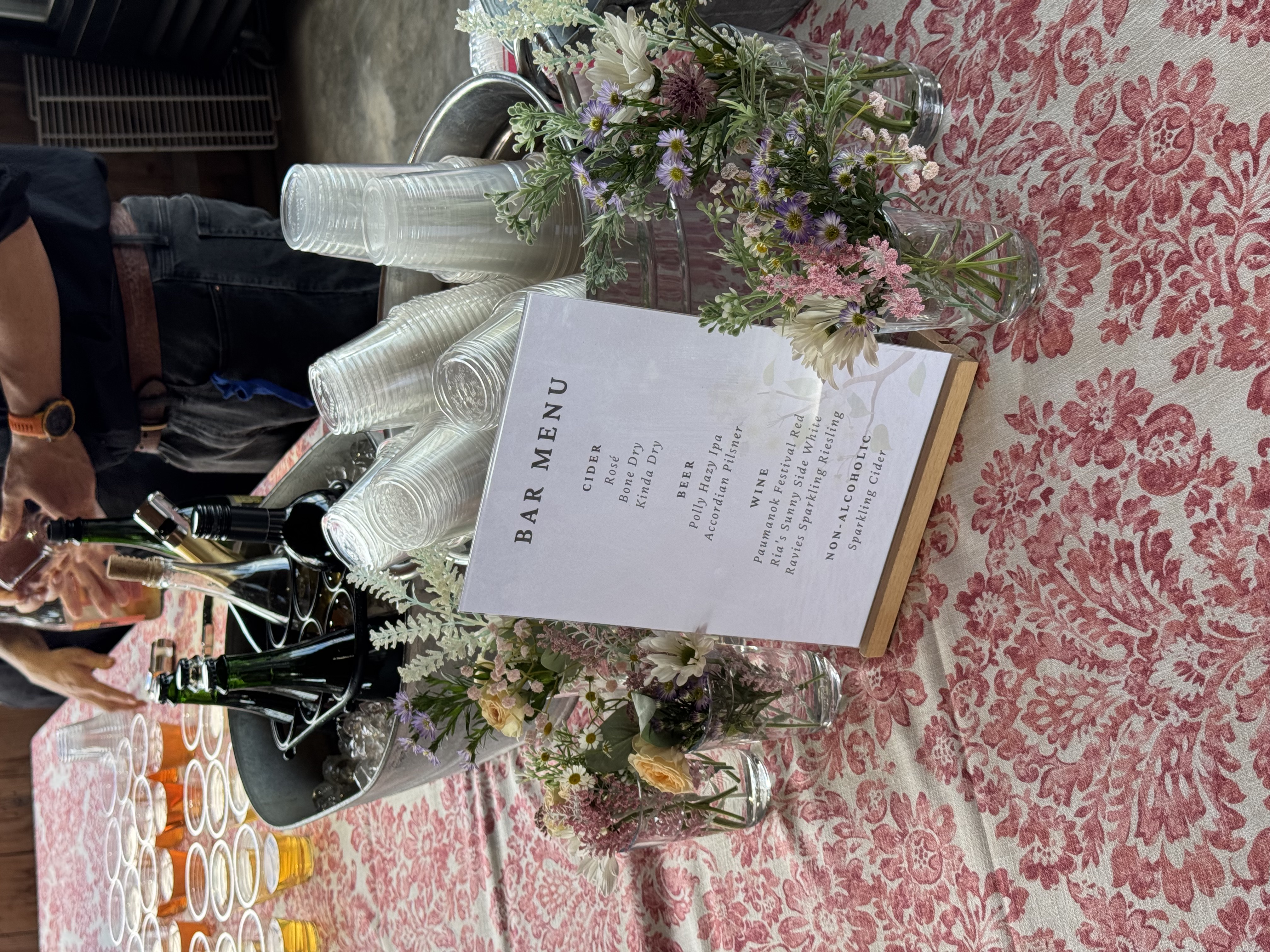 Wedding bar menu displayed with floral arrangements and beverage station at the reception